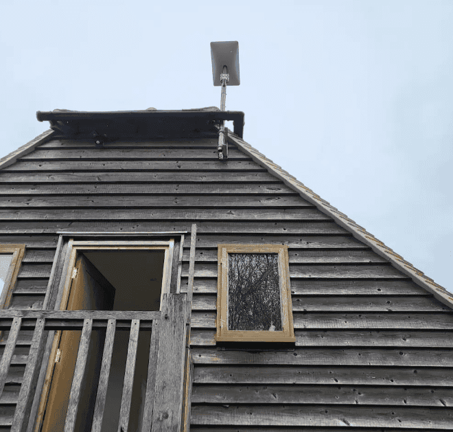 Highly experienced TV and satellite engineer installing a satellite dish on a wooden house roof in a rural area.